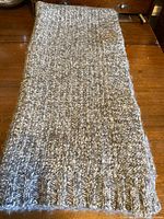 Folded wool blend hand knit blanket showing its ribbed edge and nubbly yarn texture in cloudy grey and cream tones on a wooden surface.