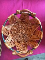 Photo showing a round wicker basket without handles featuring a pattern of wide woven bands radiating from center, with a wood-like circular frame edge.