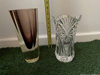 Side by side of the two vases with a measuring tape showing size comparison, green carpet background.