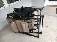 Two folded outdoor lounge chairs with black metal frames and beige fabric seats and backrests, stacked together.