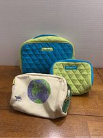 Front view of three cosmetic bags on table: two Vera Bradley quilted bags; one large blue and green, one small green and blue, and a canvas cosmetic bag featuring a globe print and Stella McCartney themed art