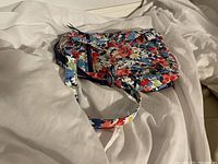 Photo of the floral patterned Vera Bradley shoulder/crossbody bag placed on white fabric showing the front and zipper details.