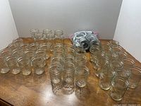 Wide shot of 41 Quilted Crystal half-pint jars, 6 pint jars, and a bag containing 48 canning lids spread on a wooden surface.