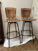 Front view of the two wooden slat swivel bar stools with metal frames showing wood slat seats and backs, black metal legs with footrests.