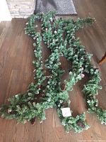 4 strands of artificial Christmas greenery garlands with pine cones laid out on wooden floor to show overall length and quantity.