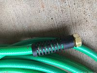 Close-up of one end of a green garden hose with brass-colored metal fitting and black rubber reinforcement.