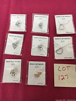 Set of 7 pins and 2 necklaces laid on red fabric background, display cards labeled with brand and price.