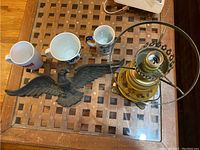Overview photo showing an eagle wall decor, four assorted mugs, and the vintage floral oil lamp.