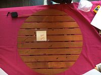 Top view of the round wooden table showing the wooden slats on the surface, placed on a red cloth.