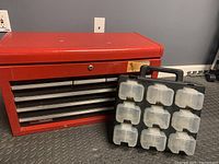 Closed red Sears Craftsman metal toolbox with locked center drawer and black plastic parts organizer with clear compartments leaning against it
