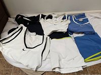 Photo showing five tennis clothing items laid out including black, white, and blue tops and white shorts.
