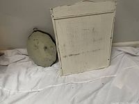 Back of white wooden wall shelf with cabinet and oval framed wall art leaning against the wall