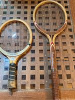 Shows two wooden rackets side by side on a wooden lattice table, views of full rackets visible.