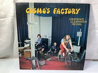 Front cover of Cosmo's Factory LP showing band members in a studio setting, album title in yellow text, artist name in yellow text on blue background.
