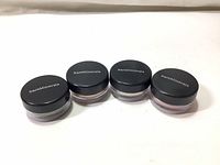 Four small round jars of loose mineral eye color makeup with black lids labeled 'bareMinerals' placed side by side on a white background.