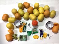 Photo showing unopened Kinder Surprise eggs in yellow, orange, and one red egg along with various miniature action figures and toy parts spread on a white background.