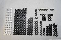 Wide overhead view showing giant lot of mostly black riflescope windage caps and some white caps organized in groups by size and quantity