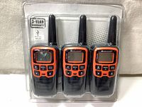 Front view of three Midland X-Talker walkie talkies in original packaging showing orange and black devices with antennas and display screens.