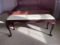 Front view of the wooden bench with upholstered cushion and visible scratches.