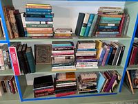 Books displayed on blue shelves arranged in different rows showing a large mixture of newer and older books across multiple subjects including history and biographies.