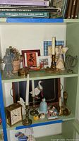 Shelf displaying brass candlesticks with candles, ceramic figurines including angel and rabbit, framed wall art, and Chelsea clock.