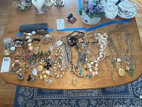Full spread of assorted costume jewelry including necklaces, bracelets, pins, watches, earrings, tie clips, and cuff links organized on wooden table