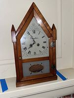 Closed view of the wooden Daneker mantel clock with Gothic pointed top, white dial with Roman numerals, and etched lower glass panel.