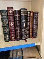 Photo showing the seven Franklin Library books lined up upright on a shelf, titles and ornate spines visible.