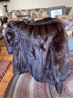 Photo of the back of the dark brown fur coat draped over a chair showing full fur texture and glossy finish.