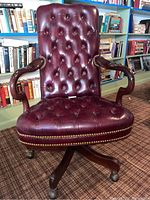 Front view of chair showing button-tufted leather backrest and seat, nailhead trim, curved wooden arms, and five-star caster base