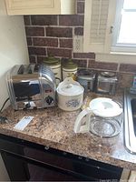 Countertop view showing toaster, two ceramic canisters, ceramic salt jar, and part of a glass coffee pot.