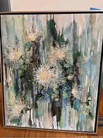 A framed canvas painting featuring white floral forms with long petals/leaves in shades of green, blue, brown, and white with dripping paint style in the background.