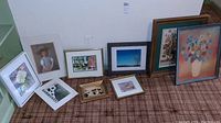 Nine pieces of wall art arranged on carpet, showing variety in subject matter including floral, animal, portrait, and landscape images