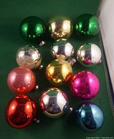 Set of 12 vintage mercury glass Christmas ball ornaments in assorted colors grouped on green background.