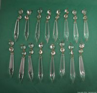 Full set of 16 icicle glass chandelier prisms arranged on a green surface.