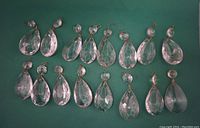 16 clear glass teardrop chandelier prisms arranged in a grid on a green surface showing both front and side views.