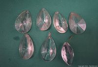 Seven tear drop shaped clear glass prisms displayed on a green background, showing their shape and reflective facets.