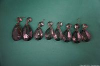 Top down view showing all 8 smoke-coloured glass teardrop chandelier prisms in a row on a green surface.