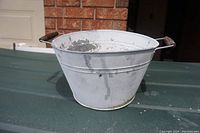 Side view of the aluminium basin planter on a dark surface, showing overall shape and condition with paint flaking visible.