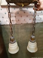 Photo of two frosted glass shades with scalloped edges hanging from metal chains, showing the condition and chip on one shade.