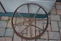 Top-down view of the antique forged iron steel wheel showing the full circular shape, eight spokes, and rusted iron surface on a paved ground.