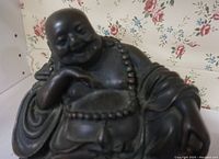 Front close-up of the Buddha statue showing smiling face, beaded necklace on neck, and robe folds on arm and body.
