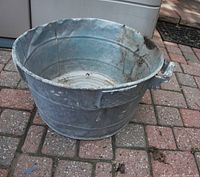 Large aluminium basin on a paved surface, showing a rough, weathered exterior and side handles.