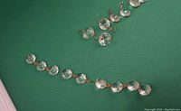 Loose small crystal chandelier pieces arranged on green surface. Octagonal clear crystals with metal hooks visible in close-up.