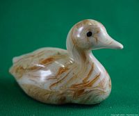 Close-up of the miniature duck figurine showing its marbled brown and beige swirled surface with black eyes.