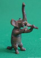 Front view of the small standing elephant figurine with raised trunk playing fiddle on green fabric background.
