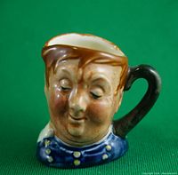 Front view of miniature Royal Doulton Toby Jug showing painted face and blue decorated coat.