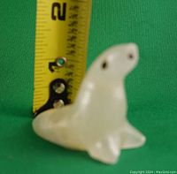 White marble seal figurine sitting upright next to a ruler for size reference