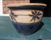 Side view of a round pottery planter showing navy blue glaze on lower half and beige upper half with raised floral decoration.