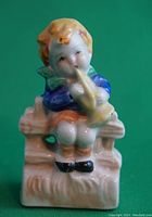 Front view of vintage porcelain miniature boy on bench playing trumpet.